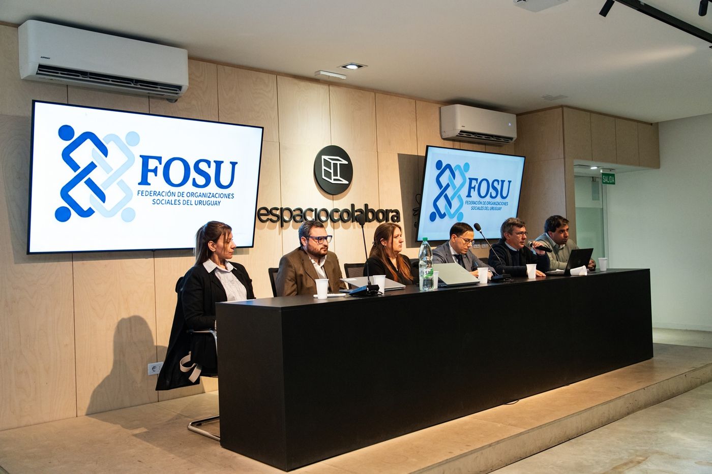 La mesa del lanzamiento oficial de FOSU, con el logo de la federación en las dos pantallas
